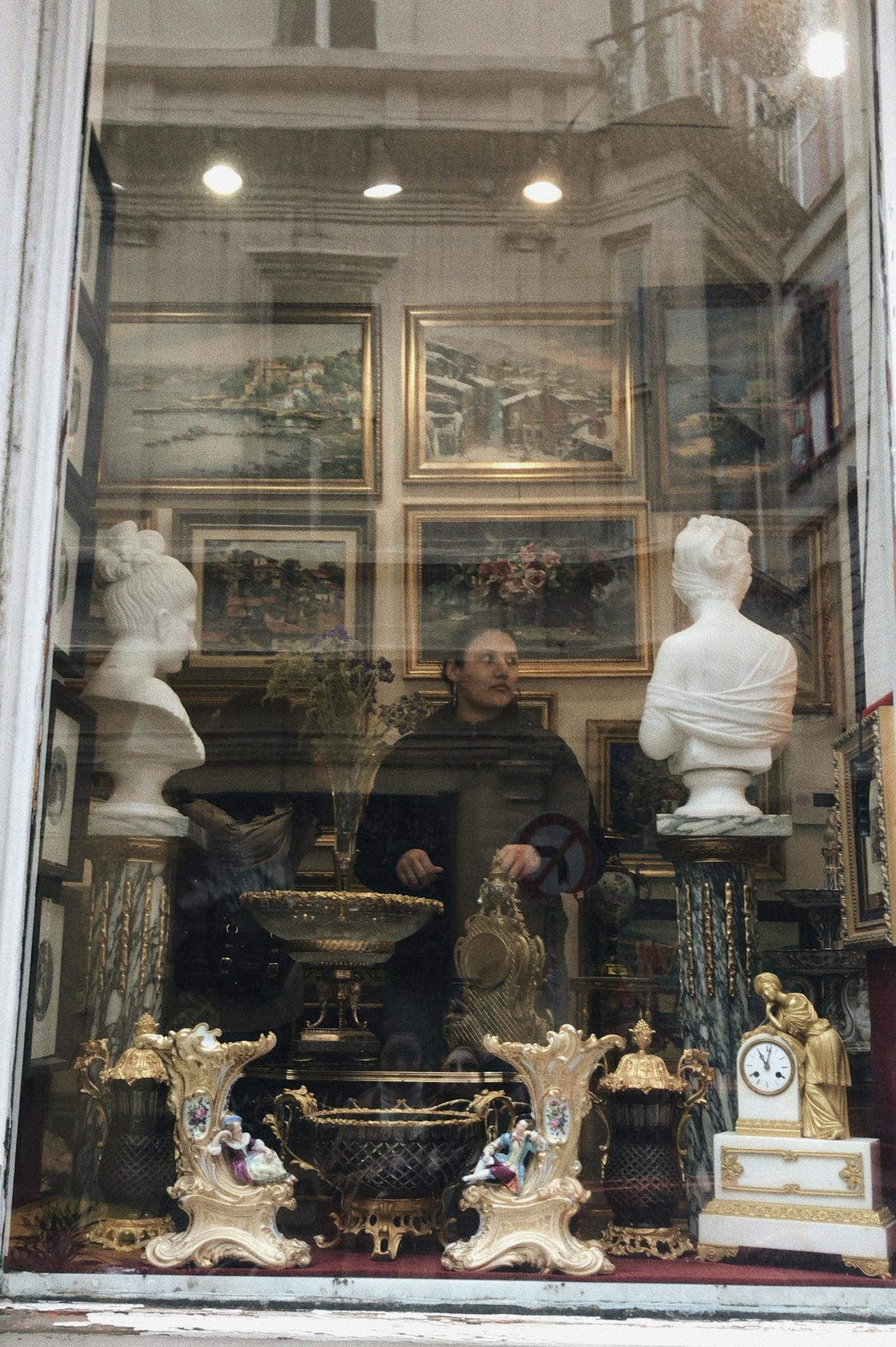 Explore an antique shop window display with sculptures, paintings, and vintage decor.
