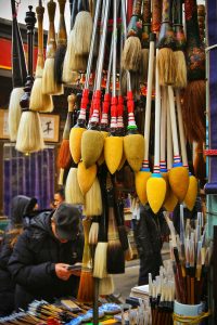 Vibrant display of handmade calligraphy brushes in a bustling Beijing market street.