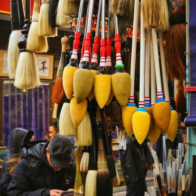 Vibrant display of handmade calligraphy brushes in a bustling Beijing market street.