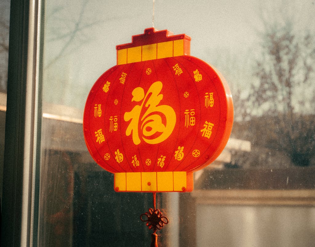 Red Chinese lantern with golden characters hanging near a window, symbolizing prosperity and celebration.
